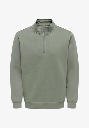 Grønn genser med glidelås og høy krage, laget av mykt stoff. Har kort glidelås foran, ribbestrikkede mansjetter og en avslappet passform.