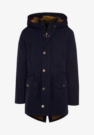 Parka bleu marine avec fermeture éclair avant, boutons-pression, taille ajustable par cordon, poches à rabat, et une capuche doublée de polaire marron et jaune.