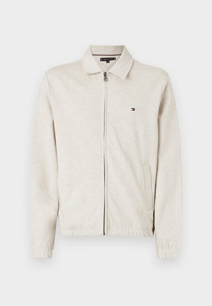 Svetlo béžová zipová bunda z mäkkého materiálu, s golierom, prednými vreckami a malým logom na ľavej hrudi.