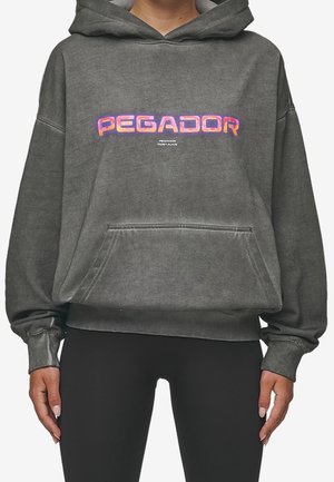 Sudadera gris de gran tamaño con un bolsillo frontal y capucha ajustable con cordón. Presenta el logo "PEGADOR" en colores vibrantes en el pecho. Tejido de mezcla de algodón.