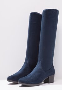 Knee-high navy blue boots made of soft textile, featuring a rounded toe and a low block heel. Smooth texture and minimal stitching details.