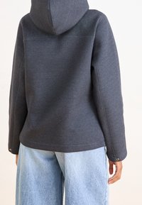 Donkergrijze hoodie met een gladde textuur, goed passende mouwen en een rechte snit. Gecombineerd met lichtblauwe wijde spijkerbroek.