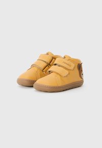 Pantofi din piele galbenă pentru copii, cu două cleme Velcro, vârf rotunjit și un accent maro la călcâi. Design pentru confort, cu o talpă flexibilă.