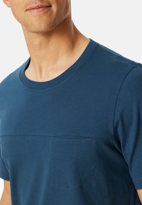 Námořnická modrá bavlněná tričko s kulatým výstřihem a malou kapsičkou na hrudi. Hladká textura a ležérní design s krátkými rukávy.