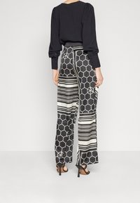 Pantalon à jambes larges avec un motif géométrique noir et blanc comprenant des hexagones et des rayures. Confectionné dans un tissu lisse, porté avec des talons hauts.