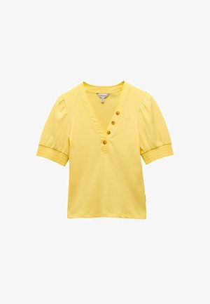 Sárga pulóver, V-nyakkal, rövid puffos ujjakkal, és öt gombbal elől. Puha anyagból készült, sima textúrával.