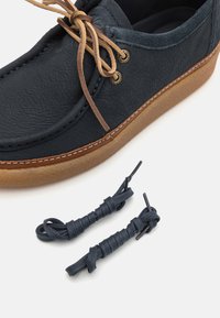 Sapato de couro azul escuro com uma superfície texturizada, sola de borracha castanha e atacadores castanhos claros. Inclui um par adicional de atacadores combinando.