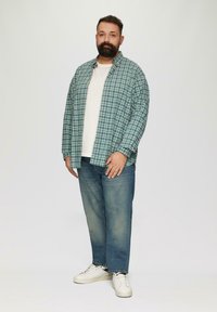 Overhemd met knopen in een geruit patroon in blauw en groen, wit t-shirt, blauwe jeans en witte sneakers. Casual, losse pasvorm met lange mouwen.