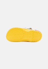 Baskets multicolores avec une semelle en caoutchouc jaune texturé, présentant un motif, une forme arrondie et une sangle ajustable.