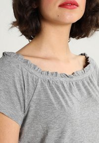 Gray cotton top with a ruffled, wide neckline and short sleeves. Soft texture and loose fit, gathered at the neckline for added detail.