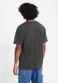 Korte mouwen, donkergrijze katoenen t-shirt met een ontspannen pasvorm, ronde halslijn en eenvoudig ontwerp. Heeft een licht verouderde stofstructuur.