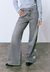 Wide-leg gray denim jeans feature a star pattern on the side. The fabric is slightly distressed with a classic five-pocket design.