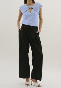 Haut bleu clair texturé avec un décolleté en trou de clé et des manches courtes, associé à un pantalon noir taille haute avec des plis et despoches latérales.