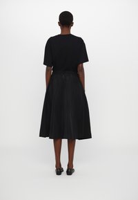 Svart T-shirt med korta ärmar kombinerad med en svart knälång kjol med elastisk midja och slät textur. Svarta platta skor.