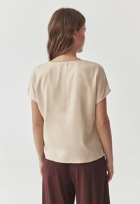 Beige lyhythihainen paita, jossa on pyöreä pääntie, sileä kangas ja rento malli; yhdistettyinä viininpunaisiin housuihin, esittelee yksinkertaista muotoilua.