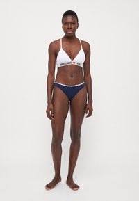 White triangle bikini top with "MOSCHINO" text; navy blue bottoms with contrasting waistband. Smooth fabric, minimalistic design, adjustable straps.