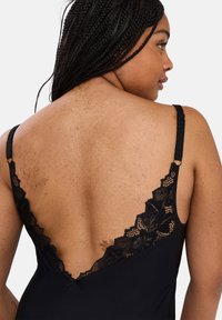 Black camisole featuring a deep V-back, adjustable straps, and floral lace trim along the neckline and back for added detail.