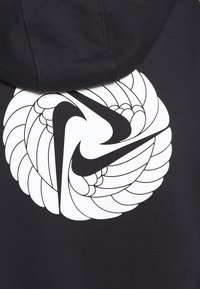 Hoodie noir arborant un grand graphique blanc d'un logo Nike stylisé entouré d'un motif de plumes tourbillonnantes. Texture de tissu lisse.