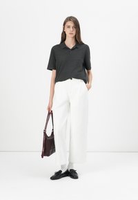 Mörkgrå polo shirt, vita vida byxor, svarta skor, håller en vinröd väska. Slät textur, klassisk design och avslappnad silhuett.