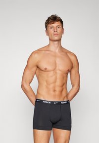 Schwarze Nike Boxer Shorts mit einem breiten weißen Bund, der das Markenlogo zeigt. Weiches Material, eng anliegendes Design, mit einer Länge bis zur Mitte des Oberschenkels und einer glatten Textur.