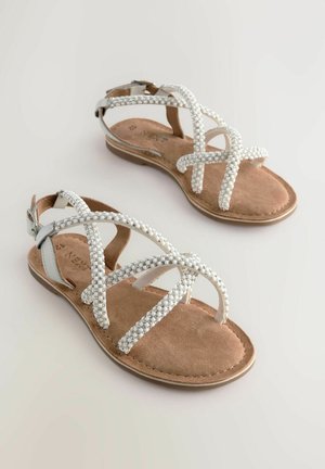 Bijele ravne sandale s križanim trakama koje sadrže detalje od bisera. Udobna smeđa unutrašnjost koja podsjeća na zec, i podesiva srebrna kopča kao naglasak.