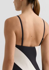 Černobílé pruhované plavky s texturovaným povrchem, nastavitelnými tenkými ramínky a hladkými látkovými detaily na okrajích.