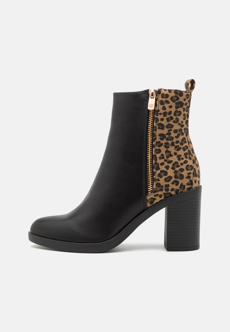 Botín con parte delantera de cuero sintético negro y parte trasera con estampado de leopardo, con una cremallera dorada y un tacón grueso negro. Textura suave en general.