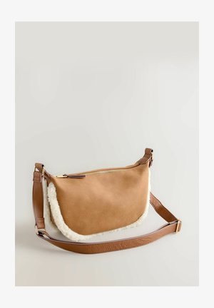 Bruine suède tas met een witte schapenvacht afwerking. Voorzien van een gouden rits en een bruine leren schouderriem. Compacte, gebogen vorm.