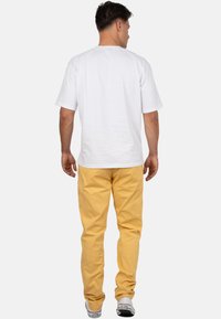 T-shirt bianco in cotone con una vestibilità comoda e maniche corte, abbinata a pantaloni gialli in cotone, vista di spalle. Sneakers visibili ai piedi.