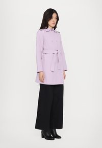 Lavendli topeltöötlusega trench coat, belti vööga, millel on krae ja pikad varrukad, koos laiad mustad püksid ja kontsakingadega.