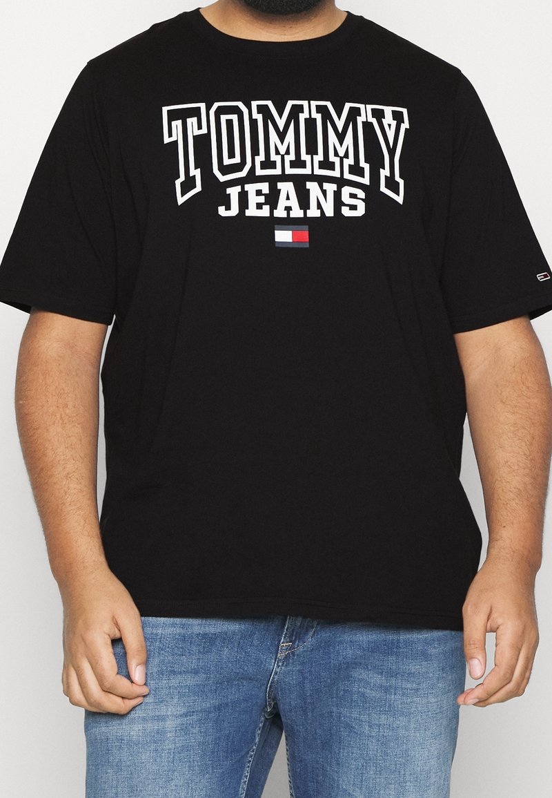 Musta puuvillapaita lyhythihaisilla, jossa on valkoisella painettu "TOMMY JEANS" ja pieni logo punaisena, valkoisena ja sinisenä. Rennosti istuva malli.