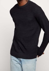 Dark knit sweater with a ribbed texture, round neckline, and long sleeves, paired with light blue jeans.