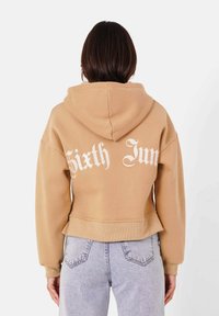 Sudadera corta marrón con capucha, que presenta el texto en blanco "Sixth Jun" en la parte posterior, confeccionada en un tejido suave con un ajuste relajado.