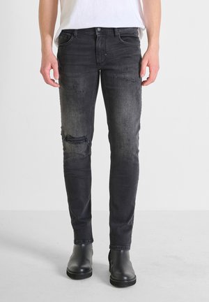 Jean skinny noir délavé avec des détails déchirés, texture usée et design traditionnel à cinq poches, associé à des bottines noires.