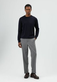 Marineblauwe trui met lange mouwen, grijze broek en bruine loafers. Casual pasvorm, gladde textuur en subtiel ontwerp voor een strakke, moderne uitstraling.