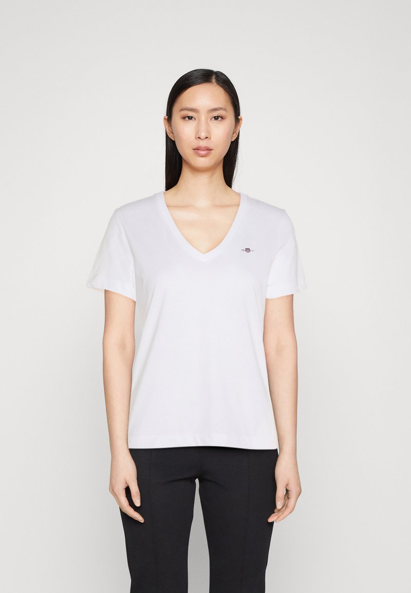 Hvid V-hals T-shirt med korte ærmer, lavet af blødt stof, prydet med et lille broderet logo på venstre bryst, minimalistisk design.