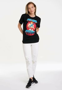 Black cotton T-shirt featuring a colorful He-Man graphic. Paired with white pants and black athletic shoes with white stripes.
