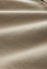 Tissu en coton beige avec une texture lisse, présentant un motif en maille fine et un léger éclat, plié pour montrer son tombé et sa douceur.
