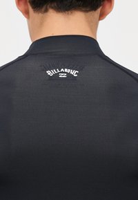 Fekete, hosszú ujjú rash guard, sima tapintással. A hátsó felső részen fehér "Billabong" logó található, valamint kontrasztos varrás.