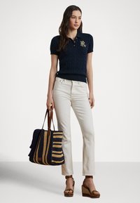 Námornícka krátky rukáv pletená polo košeľa s logom, skombinovaná s krémovými džínsami rovného strihu a prúžkovanou tkanou taškou. Hnedé klinové sandále.