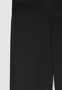 Zbliżenie na czarną tkaninę z szwem biegnącym wzdłuż środka, pokazujące część odzieży, prawdopodobnie spodni lub spódnicy, na jasnoszarym tle.