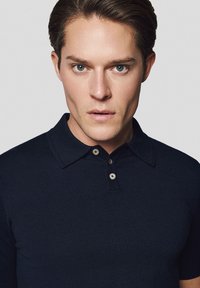 Granatowa koszulka polo z krótkim rękawem wykonana z teksturowanej dzianiny, z kołnierzykiem typu spread i zapięciem na dwa guziki.