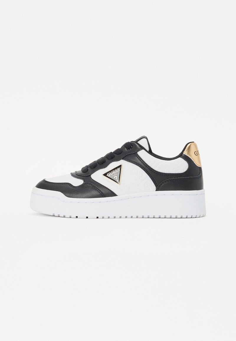 Baskets basses noires et blanches avec une semelle blanche épaisse, des lacets noirs, un logo triangulaire sur le côté et un accent doré au talon.