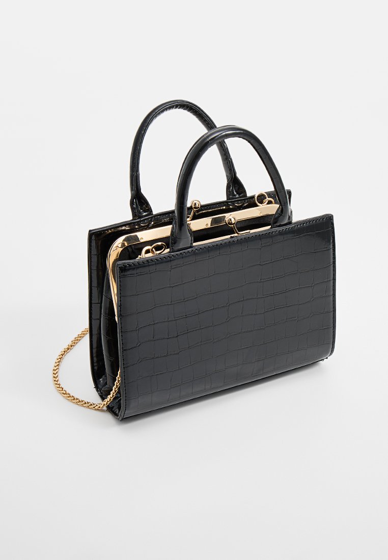 Sac à main en cuir synthétique noir avec une texture crocodile, deux poignées supérieures, un fermoir doré et une bandoulière en chaîne amovible.
