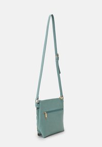 Crossbody-väska i texturerat turkossyntetmaterial. Har en ficka med guldfärgad dragkedja fram och en justerbar axelrem.