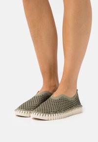 Olivengrønne slip-on sko med en tekstureret, åndbar overdel og hvid gummisål med en sålrand.