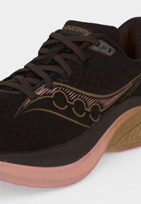 Σκούρο καφέ αθλητικό παπούτσι Saucony με μαύρες και ροζ λεπτομέρειες, καφέ κορδόνια και παχιά καφέ και ροζ σόλα.