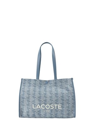 Sac cabas en denim bleu avec motif losange, deux bretelles, fermeture à bouton, et "LACOSTE 1933" imprimé sur le devant.
