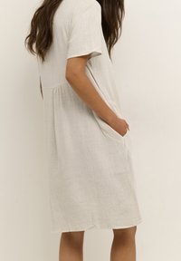 Robe légère en lin de couleur beige neutre, dotée de manches courtes, d'une coupe décontractée, d'une couture à la taille et de poches latérales. Texture lisse avec un tissage subtil.