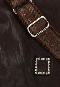 Borsa in pelle marrone con una tracolla intrecciata caratterizzata da strisce marroni, fibbia rettangolare in argento e un patch decorativo con borchie.